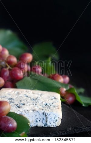 Blue cheese Dorblu with red grape on black background