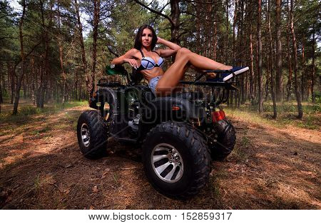 Elegant woman sitting on quadrocycle ATV in forest
