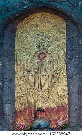 Vadipatti India - October 22 2013: Closeup of golden Virgin Mary fresco in a grotto at Vadipatti Arockia Annai Shrine. She holds rosary and stands on the head of black snake. Image of god and angels.