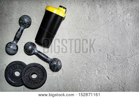 Fitness or bodybuilding concept background. Product photograph of old iron dumbbells and shaker on grey, conrete floor in the gym. Photograph taken from above, top view with lots of copy space