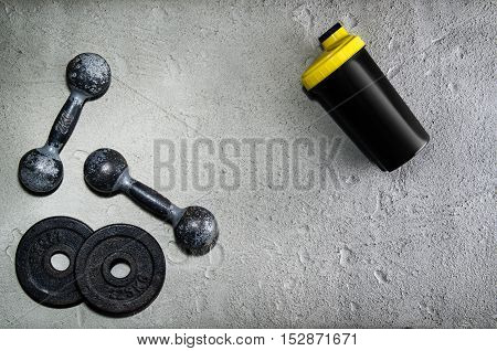 Fitness or bodybuilding concept background. Product photograph of old iron dumbbells and shaker on grey, conrete floor in the gym. Photograph taken from above, top view with lots of copy space
