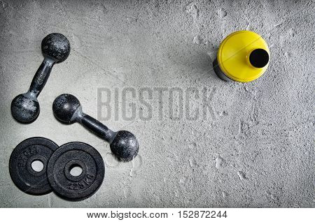 Fitness or bodybuilding concept background. Product photograph of old iron dumbbells and shaker on grey, conrete floor in the gym. Photograph taken from above, top view with lots of copy space