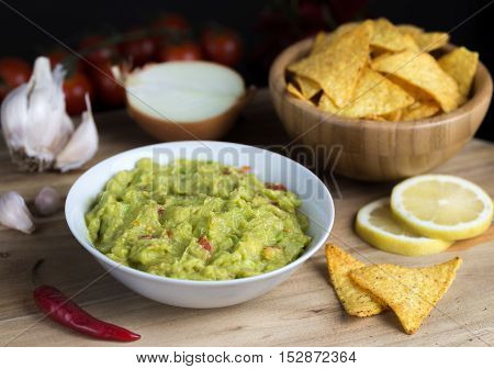 Guacamole in white bowl on natural wooden desk with tortilla chips.