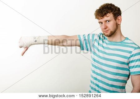 Bad news and information. Medicine aspects. Sad unhappy male with bandaged hand showing thumb down sign symbol.