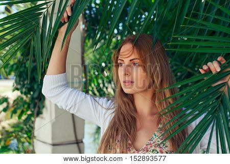 Beautiful caucasian girl on a vacation looking through palm leafs summer day