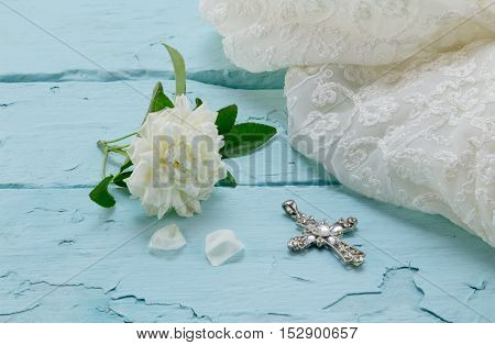 Cream rose cream lace dress and crystal cross on rough painted wood background