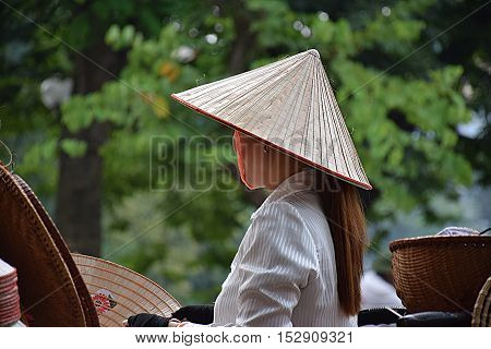 Close-up of a Vietnamese girl selling traditional hats on the streets of Hanoi old quarter, Vietnam