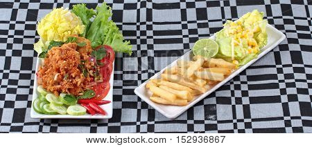Spicy sour fried chicken salad (Yum Kai Zap in Thai) served with a dish of mixed vegetables salad and french fires.