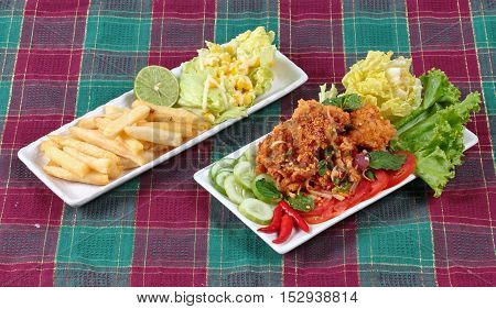 Spicy sour fried chicken salad (Yum Kai Zap in Thai) served with a dish of mixed vegetables salad and french fires.