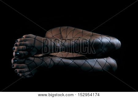 Low key special toned photo of long beautiful sexy female legs in net stockings against dark background