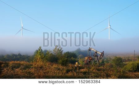 An old oil pump jack in front of modern wind turbines