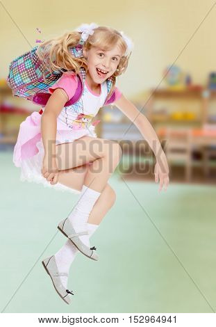 Cheerful little girl in a pink short skirt hurries to school.In the background children's room where there are shelves with toys.