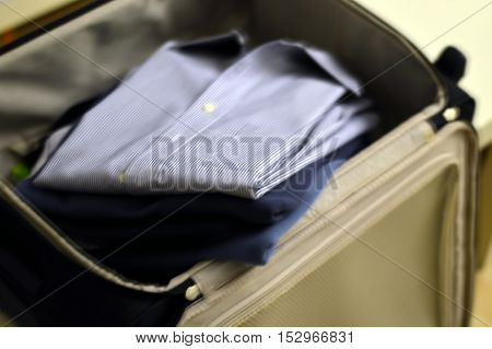 A business shirt and two sweaters in a suitcase blurred background