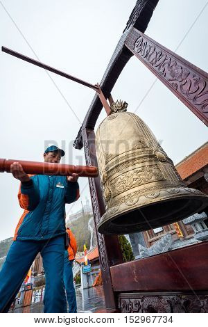 Sa Pa Vietnam - September 18 2016: Staff man in blue uniform ring a big golden bell in front of temple of Fansipan legend of Sa Pa Vietnam.
