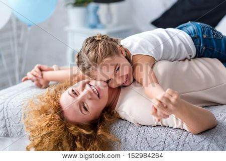 We love each other. Cheerful little girl lying on her grandmother and holding hands while having fun at home
