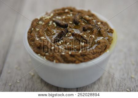 A White Bowl Of Hummus Fortified With Protein Rich Cricket Flour, And Topped With Sesame Seeds And O
