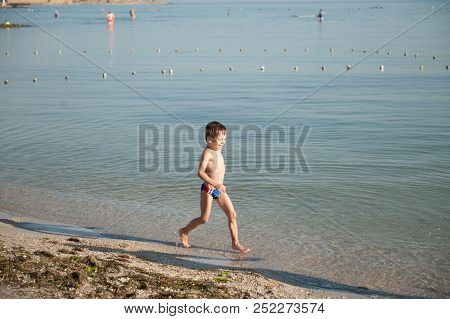 Happy Laughing Boy Running Along Ocean Coast On Sand On Beach In Summer