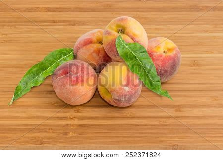 Several Ripe Fresh Peaches With Leaves On A Bamboo Wooden Surface