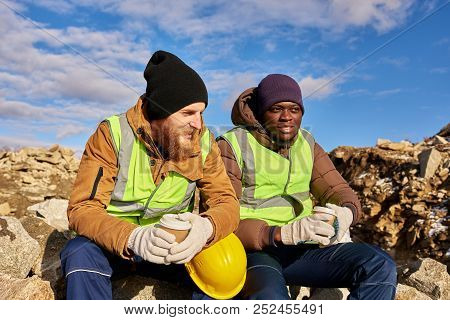 Portrait Of Two Industrial  Workers Wearing Reflective Jackets, One Of Them African, Relaxing Taking
