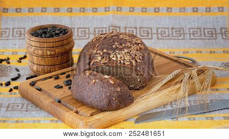 Fresh Whole-grain Bread With Seeds Cut On A Wooden Board, A Knife, Mortar With Sunflower Seeds And R