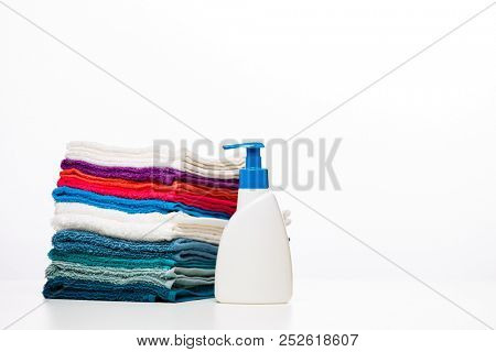 Photo of one bottle of liquid soap and colored towels on clean white background