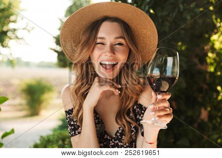 Image of pretty young woman sitting in cafe outdors in park holding glass drinking wine.