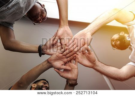 Closeup Of Young Friends With Their Hands Stacked Together Over White Background.