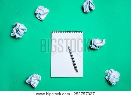 White Notebook With Pen On A Green Background Among Paper Balls. The Concept Of Generating Ideas, In