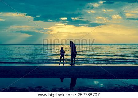 Mother And Son Relaing On The Beach During Sunset On Vacation.