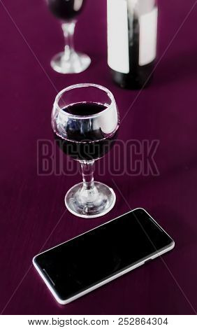 Bottle And Two Glasses Of Red Wine And A Mobile Phone On Marsala Color Wodden Table And Blurred Back