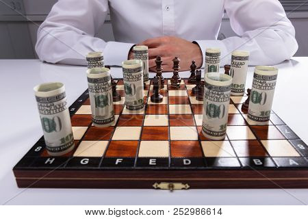 Businessman Playing Chess With Chess Piece And Rolled Up American Banknotes