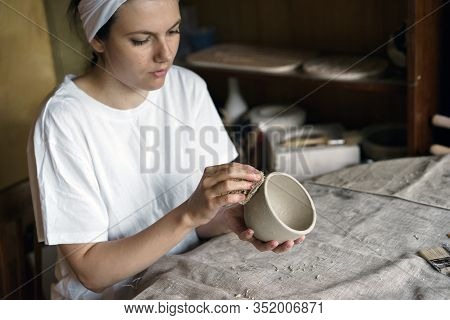 Beautiful Woman In A Creative Workshop Sits At A Table And Wipes A Clay Bowl