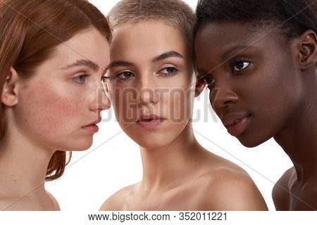 Portrait Of Three Beautiful Multicultural Young Women Standing Close To Each Other In Studio Against