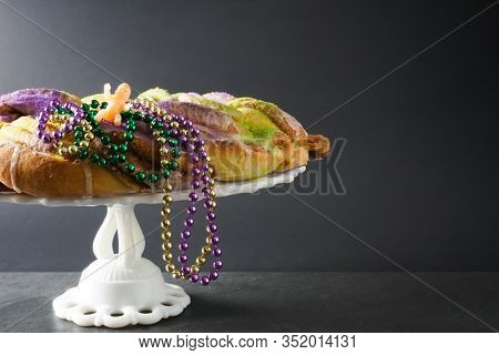 Festive Gold, Green, And Purple King Cake For Mardi Gras With Traditional Beads And A Baby Figurine;