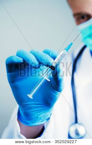 Close Up Hand Of Doctor In Blue Latex Glove And Medical Gauze Mask With Transparent Syringe. Health 