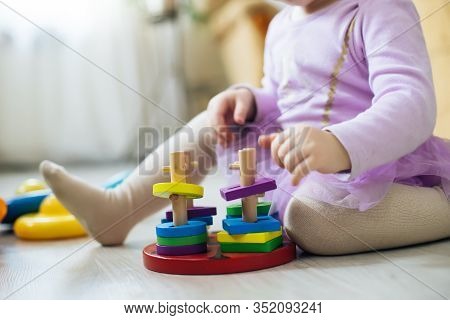 Girl Plays Toys In Living Room. Montessori Wooden Toy Folded Pyramid. Circle, Quadra, Triangle, Rect