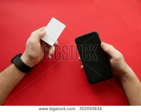 Hand With Smart Watch Holding White Card And Smartphone On Red Background. Cashless Payment, Online 
