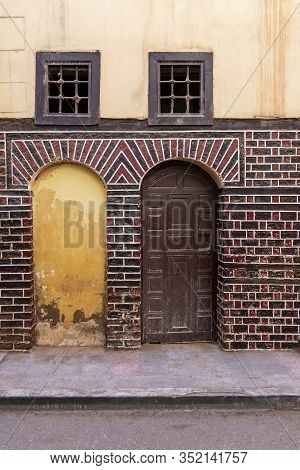 Stone Blocked Arced Door, Decorated Wooden Arched Door, And Two Small Windows With Iron Rusted Bars 