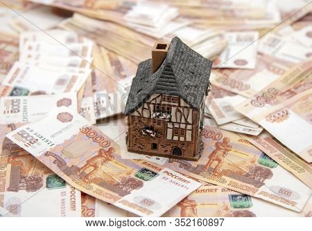 A Ceramic House Stands On A Pile Of Five Thousand Ruble Bills. Symbol Of Success, Improvement Of Liv