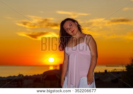 Woman In A White Dress On A Background Of The Sea At Sunset.