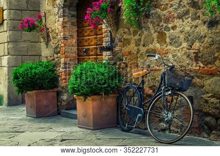 Old Fashioned Retro Bicycle Parked In The Street. Entrance And Wooden Door Decorated With Flowers An