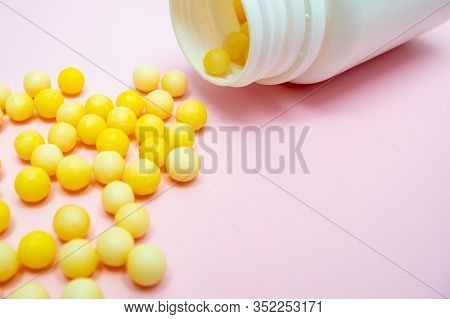 Yellow Round Dragees Of Vitamin C, Ascorbic Acid Near A White Plastic Bottle, Container On Pink Back