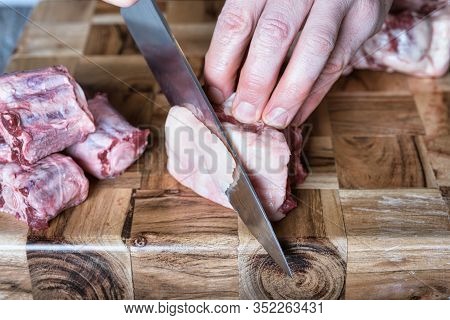 A Man Trimming Fat Off A Piece Of Ox Tail Meat With A Knife On A Cutting Board