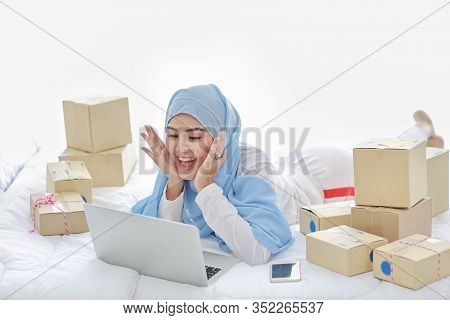 Beautiful And Young Asian Muslim Woman In Sleepwear With Attractive Look, Lies On Bed With Computer,