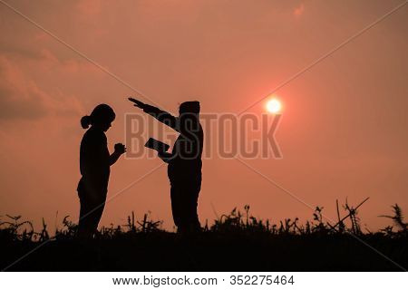Silhouette Of Two Teen Girls Praying To God With The Bible.