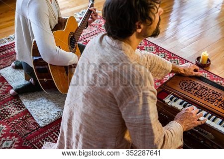 Young Man And Woman On Carpet Playing Classical Guitar And Harmonium Together As Kirtan Music For Pe