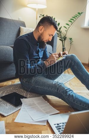 Caucasian Businessman With Long Beard Is Sitting On The Floor And Working With Some Documents Using 