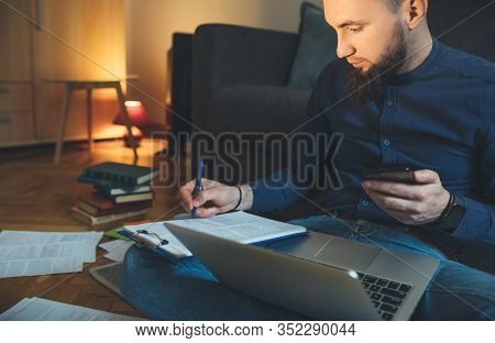 Concentrated Caucasian Businessman With Long Beard Is Writing Something While Using A Laptop And His
