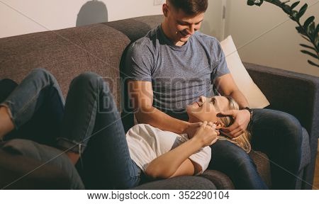 Cheerful Blonde Girl Lying On Her Caucasian Lover Dressed In Jeans And T-shirt While Looking Into Hi