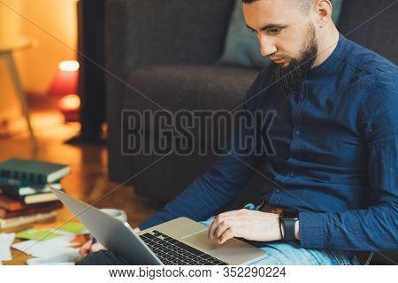 Concentrated Caucasian Man Dressed In A Blue Shirt And Wearing A Nice Beard Is Working At His Comput
